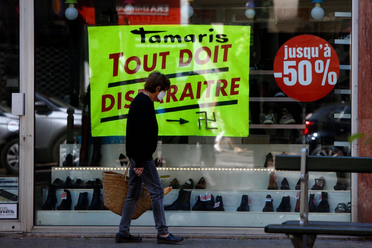 Een vrouw met mondkapje op loopt tijdens de lockdown in Parijs langs een winkelruit die ontsierd is met een hakenkruis.