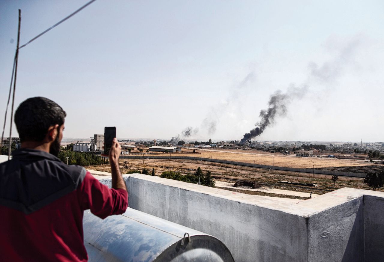 Een man fotografeert vanuit Turkije de gevolgen van de Turkse bombardementen bij de stad Ras al-Ain in het noord-oosten van Syrië.