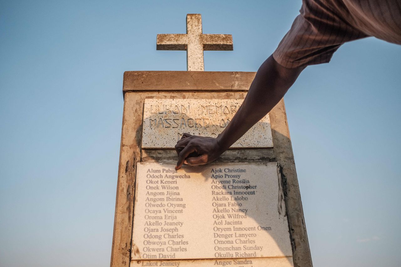 Olanyia Mohammed (38), die in 2004 aan de massaslachting van zijn dorp wist te ontkomen, wijst naar de namen van zijn ouders op een monument ter nagedachtenis van de slachtoffers in Lukodi, Oeganda.