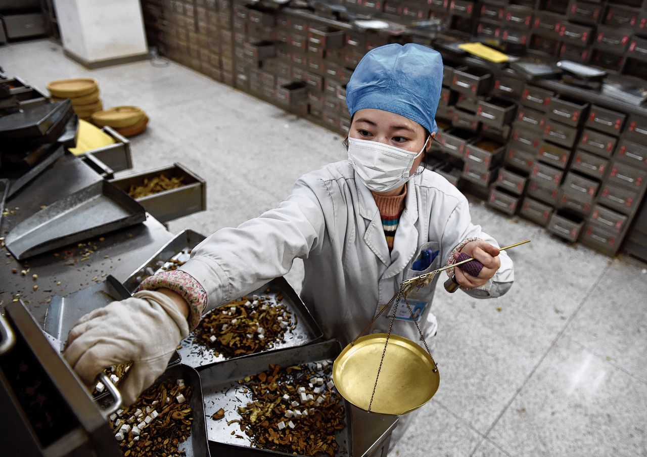 Een apotheker in de Oost-Chinese provincie Anhui mengt traditionele Chinese medicijnen bedoeld voor de behandeling van corona. Onder: een apotheek voor traditionele geneeskunde in het Chinese noordwesten.