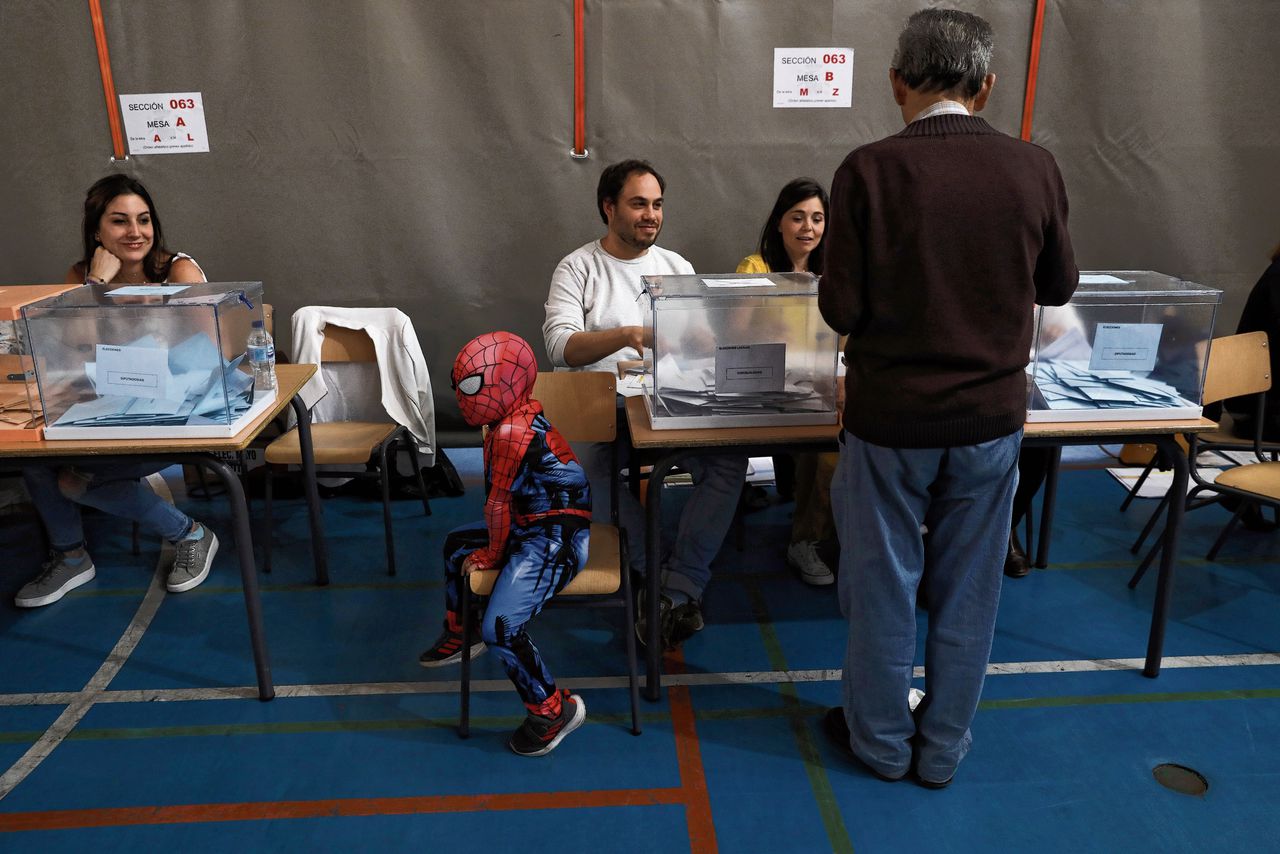 In een Madrileens stemlokaal wacht een Spaans kind in Spider-Mankleding op zijn registrerende familieleden.