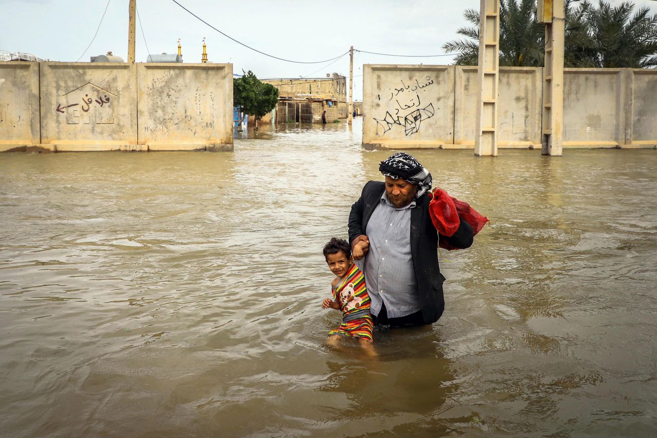 Een Iraanse man tilt zijn zoontje door het water in zijn overstroomde dorp nabij de stad Ahvaz.