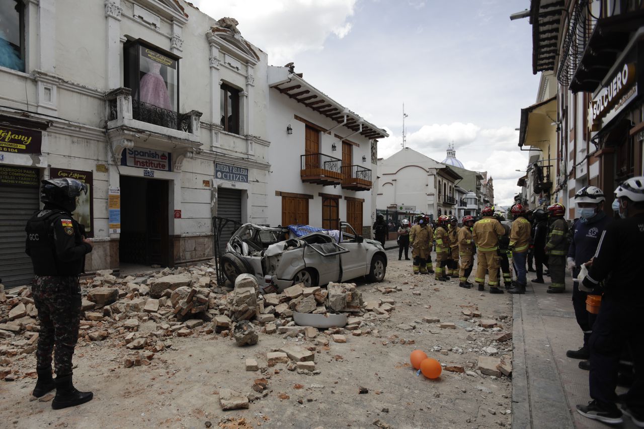 Reddingswerkers staan zaterdag in de Ecuadoriaanse stad Cuenca bij een auto die is getroffen door vallend puin als gevolg van een aarbeving.
