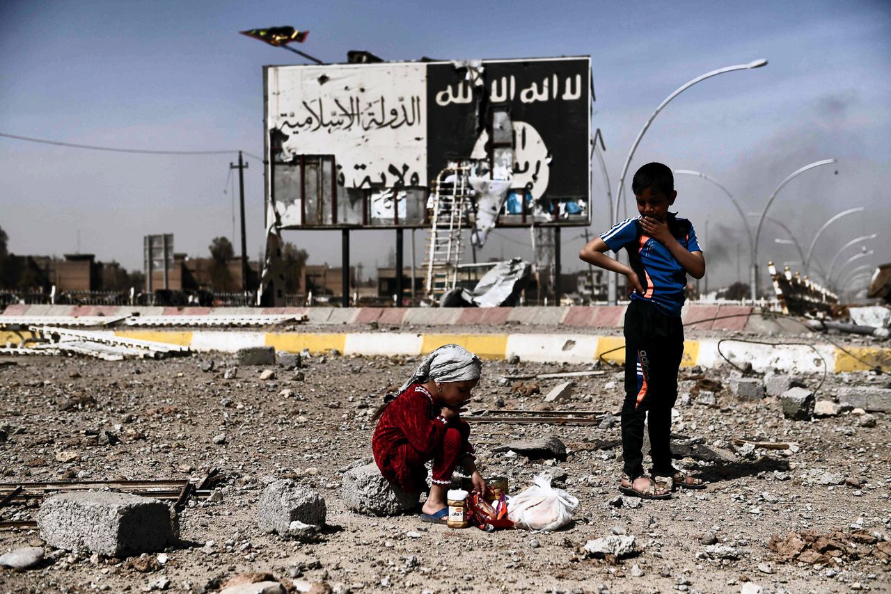 Iraakse kinderen tussen het puin in Mosul op 12 maart 2017. Op de achtergrond is het logo van Islamitische Staat te zien.
