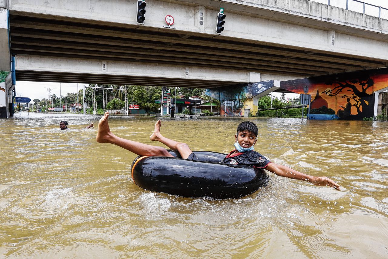 Een kind in Sri Lanka gebruikt een opblaasbare band om zich te verplaatsen door een overstroomde straat in Colombo.