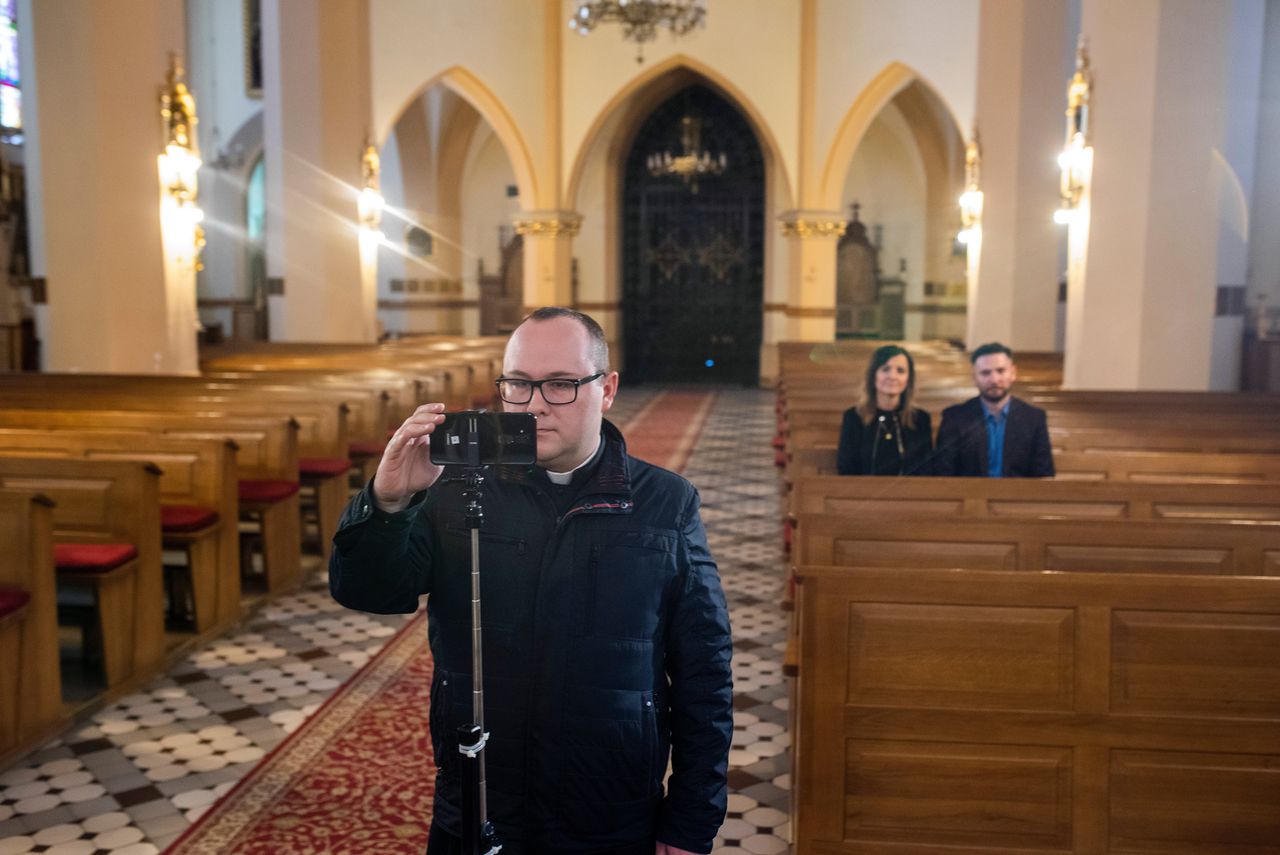 Vicaris Sebastian Szkop bedient de smartphone waarmee de missen in Charlupia Mala gelivestreamed worden.