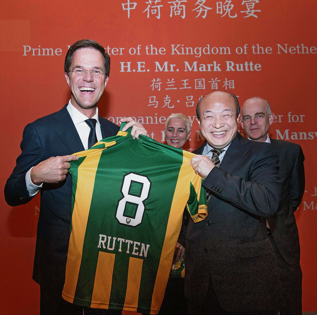 Premier Rutte houdt een shirt van ADO Den Haag omhoog – met daarop zijn verkeerd gespelde naam. Hij kreeg het tijdens de handelsmissie van de Chinese eigenaar van ADO, Wang Hui (r).