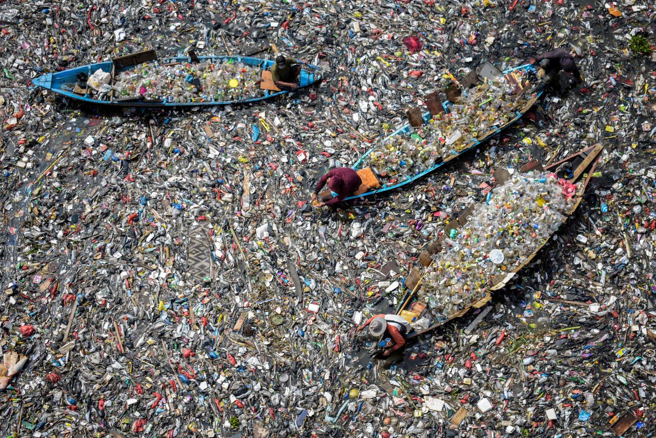 Mensen op boten halen recyclebaar plastic uit de zeer vervuilde rivier de Citarum in Bandung, West-Java.