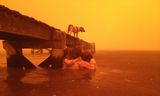 In this Jan. 4, 2013, photo provided by the Holmes family,  Tammy Holmes and her grandchildren take refuge under a jetty as a wildfire rages nearby in the Tasmanian town of Dunalley, east of the state capital of Hobart, Australia. The family credits God with their survival from the fire that destroyed around 90 homes in Dunalley. Record temperatures across southern Australia cooled Wednesday, Jan. 9, 2013, reducing the danger from scores of raging wildfires but likely bringing only a brief reprieve from the summer’s extreme heat and fire risk. (AP Photo/Holmes Family, Tim Holmes) EDITORIAL USE ONLY