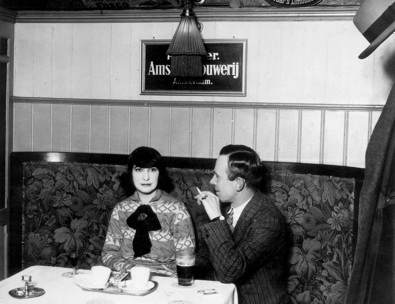 Schrijfster Mary Dorna, auteur van onder meer Laten we vader eruit gooien, in een café naast een rokende man, circa 1930.