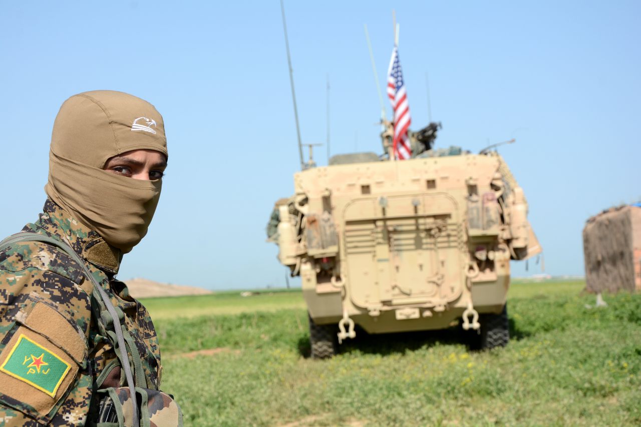 Een Koerdische strijder van de YPG naast een Amerikaanse tank vlakbij de Syrisch-Turkse grens.