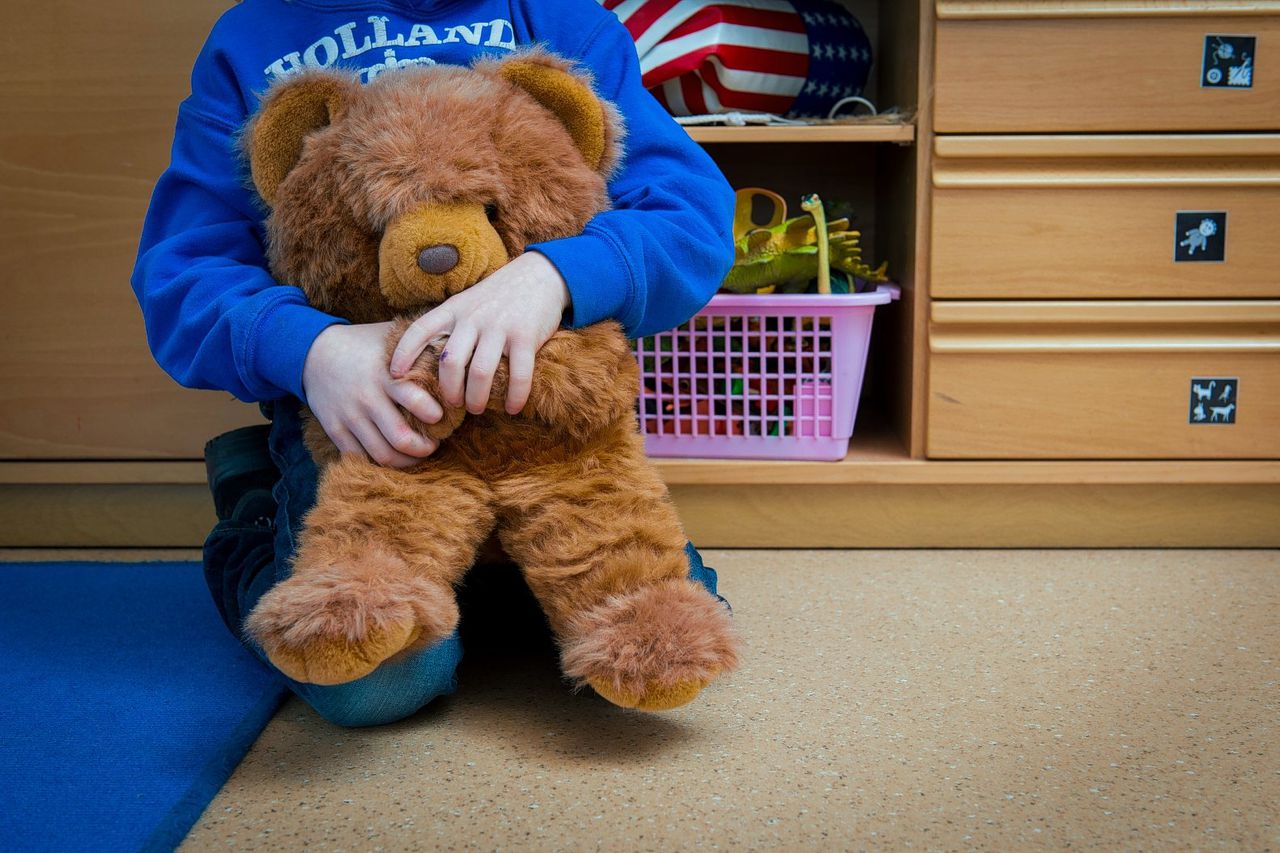 Een jongen met een knuffelbeer in een speelkamer van een jeugdhulpverleningscentrum.