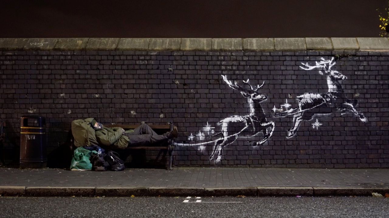 Een man op een bank bij Banksy’s nieuwe Kerst-muurschildering in Birmingham. Foto uit Banksy’s Instagram-filmpje.