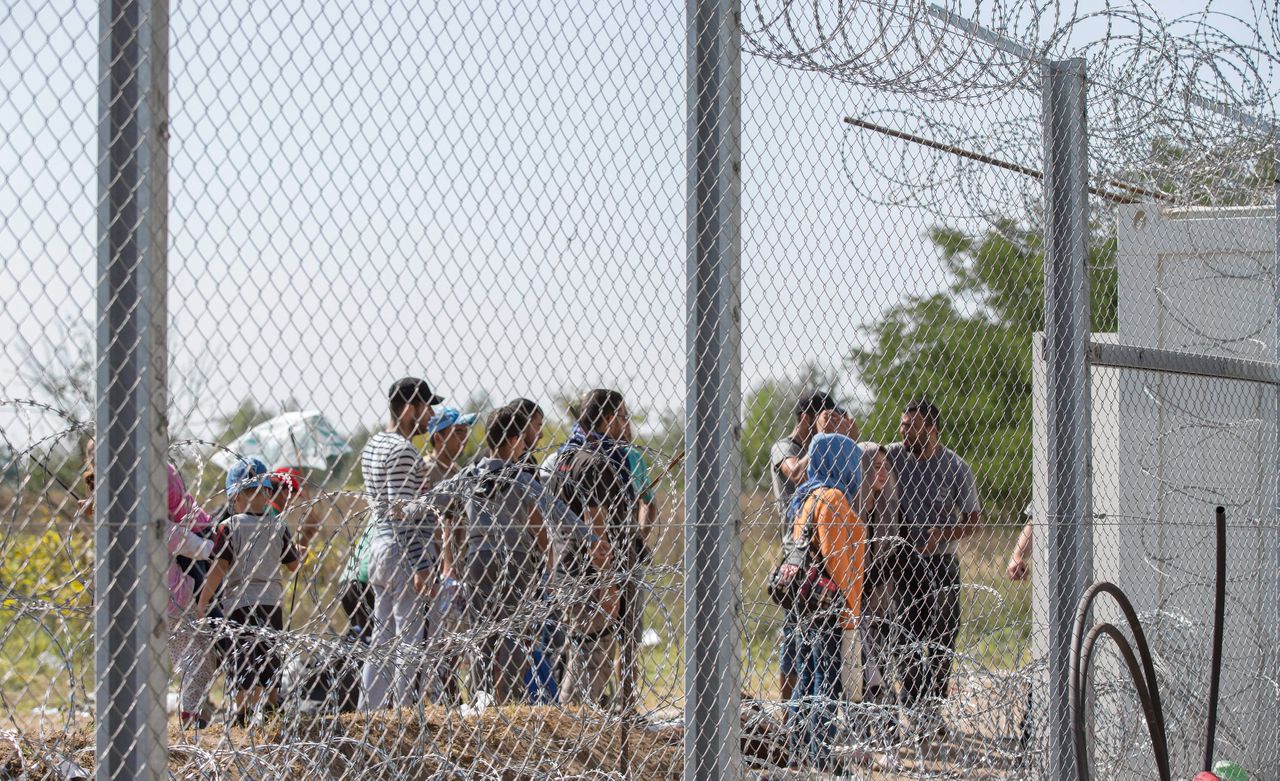 Migranten wachten tot ze het hek bij Röszke aan de Servisch-Hongaarse grens doorgelaten worden.