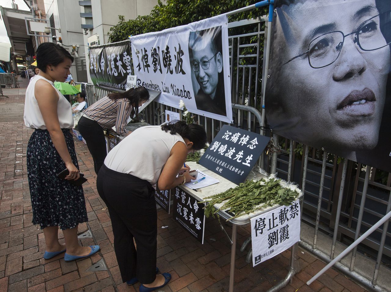 Iemand schrijft iets in het condoleanceregister en legt bloemen als betuiging van respect aan Xiaobo.