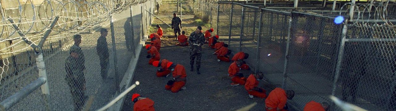 Detainees in orange jumpsuits sit in a holding area under the watchful eyes of military police during in-processing to the temporary detention facility at Camp X-Ray of Naval Base Guantanamo Bay in this January 11, 2002 file photograph. A cache of classified U.S. military documents provides intelligence assessments on nearly all of the 779 people who been detained at the Guantanamo Bay prison in Cuba. The secret documents, made available to The New York Times and several other news organizations, reveal that most of the 172 remaining prisoners have been rated as a "high risk" of posing a threat to the United States and its allies if released without adequate rehabilitation and supervision, the newspaper said in its report late on April 24, 2011. REUTERS/Stringer/Files (CUBA - Tags: CRIME LAW POLITICS)