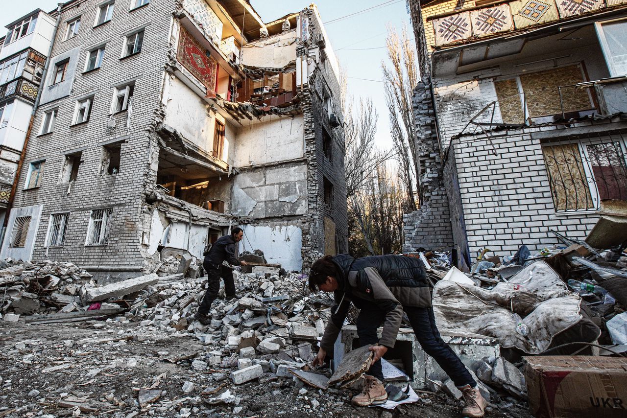 Ira en Igor Filesj verzamelen hout in het puin van een flatgebouw in Mykolajiv dat is verwoest bij een Russische raketaanval.