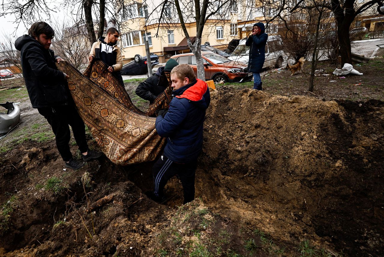 Inwoners van Boetsja dragen dinsdag het lichaam van een omgekomen man om hem in een tuin te begraven.