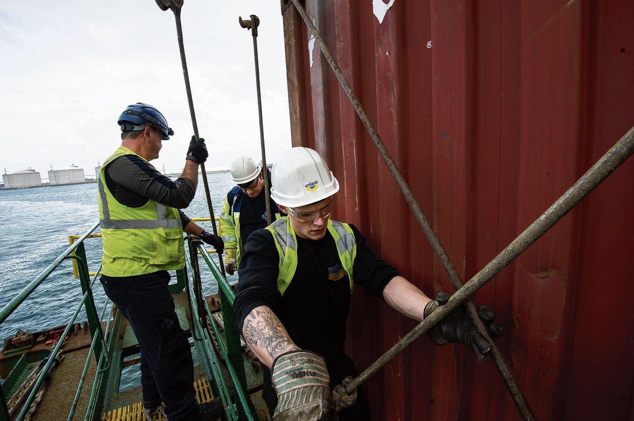 ‘Sjorders’ maken zeecontainers aan elkaar vast met zware stalen stangen, op een schip in de Rotterdamse haven.