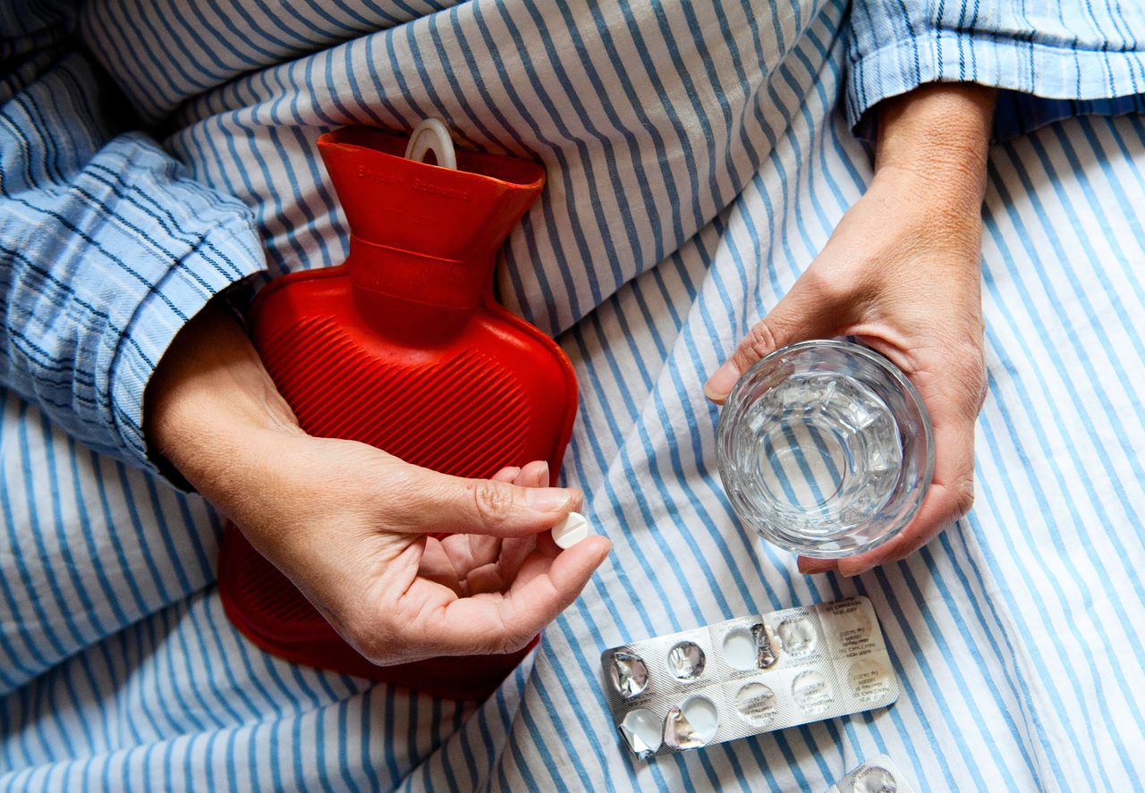 Een vrouw in bed neemt paracetamol.