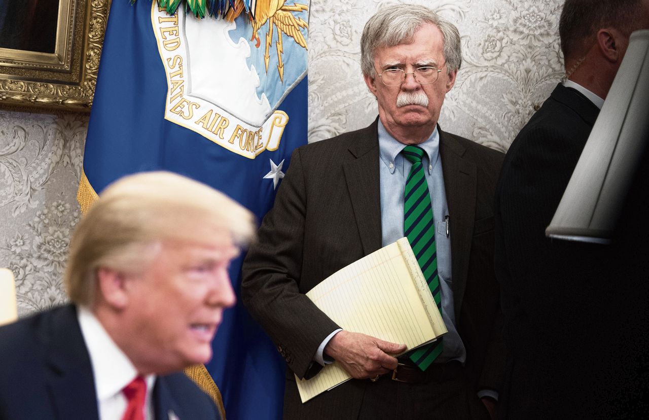 Bolton, met notitieblok, luistert naar Trump in het Oval Office in mei 2018.