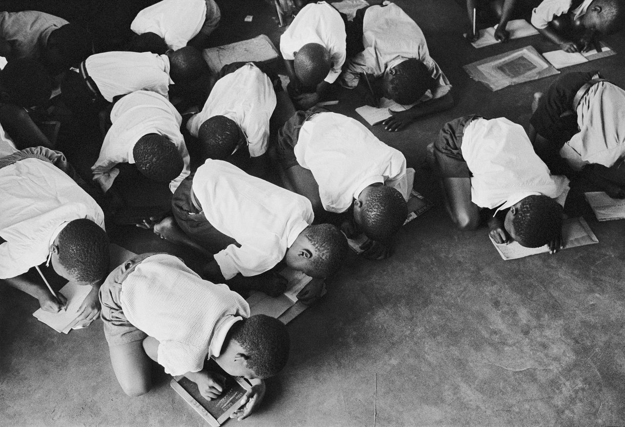 Zuid-Afrikaanse leerlingen zitten geknield op de vloer tijdens de schrijflessen. (Zuid-Afrika, jaren 60).