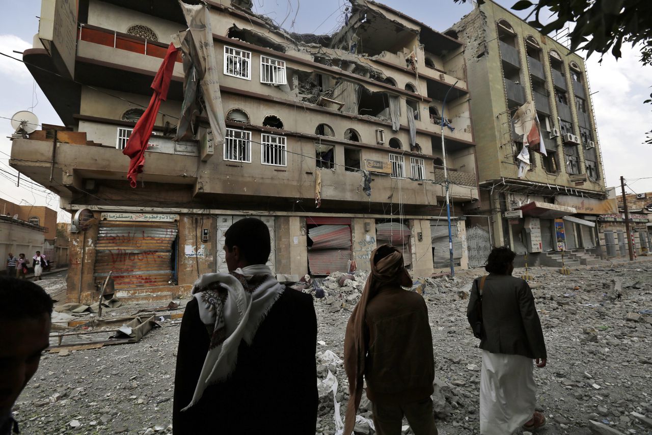 Jemenitische burgers kijken naar gebouwen in Sana'a die zijn verwoest door luchtaanvallen van de internationale coalitie geleid door Saoedi-Arabië.