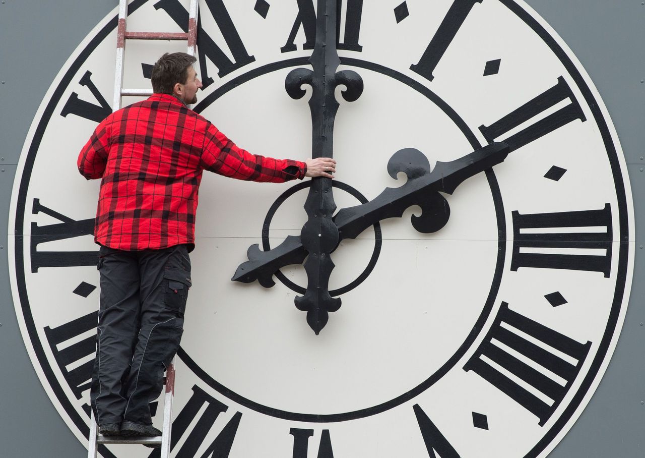 Een man draait handmatig de klok een uur terug. In Marokko hoeft dat niet meer te gebeuren.