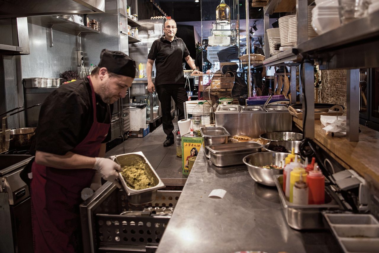 Het Syrische restaurant Sham in de Warmoestraat werkt met vrijwel alleen Syrische vluchtelingen in de keuken en de bediening. Eigenaar Momen Al-Azhar van oorsprong ook Syrisch woont al 30 jaar in Nederland. Op de achtergrond kok Omar Bakbounsi (ook in het verhaal) aan het werk in de keuken.