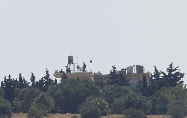 A group of people with a machine gun take position on top of a building near mountains on the Syrian side of the border zone between Syria and Turkey, near the Turkish village of Guvecci, 50 kilometres (31 miles) from Hatay province June 23, 2011. REUTERS/Umit Bektas (TURKEY - Tags: POLITICS CIVIL UNREST MILITARY)
