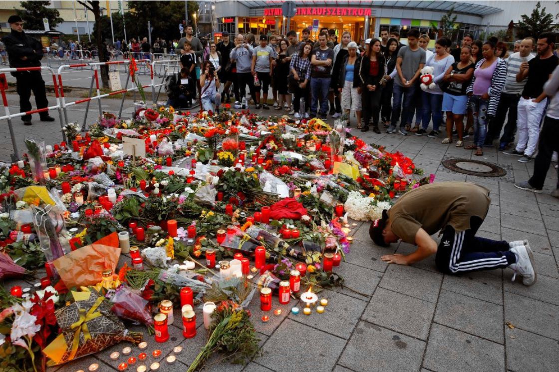 Een man bidt bij de bloemenzee voor het winkelcentrum in München waar vrijdag de schietpartij plaatsvond.