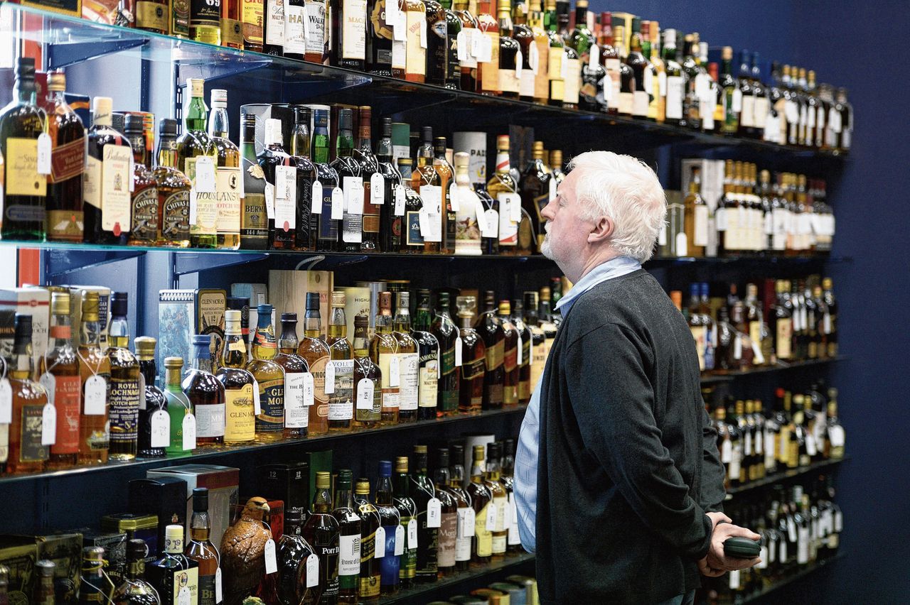 Een verzamelaar bekijkt het aanbod van whisky’s in een Schots veilinghuis.