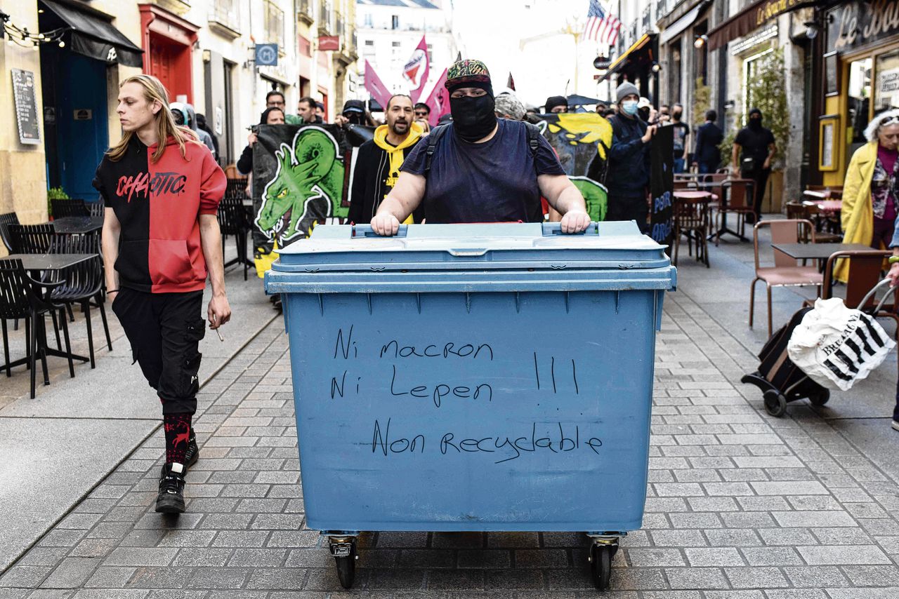 Een demonstrant duwt een afvalbak met de tekst „Noch Macron, noch Le Pen, niet recyclebaar” bij een betoging in Nantes op 16 april (boven); Macron plakt de Franse vlag op een windturbine in Le Havre (onder).
