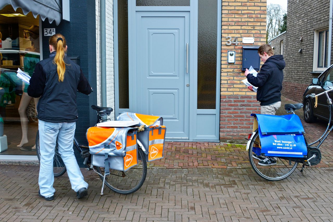 Een postbezorger van Postnl en Sandd passeren elkaar tijdens hun ronde om poststukken te bezorgen.