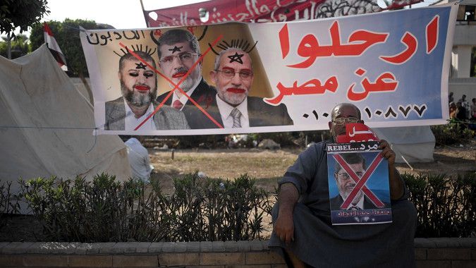 Een tegenstander van Mohammed Morsi, afgelopen vrijdag buiten het ministerie van Defensie in Kairo, bij een banier met daarop vlnr. Kairat el-Shater,Morsi, en Mohammed Badie.