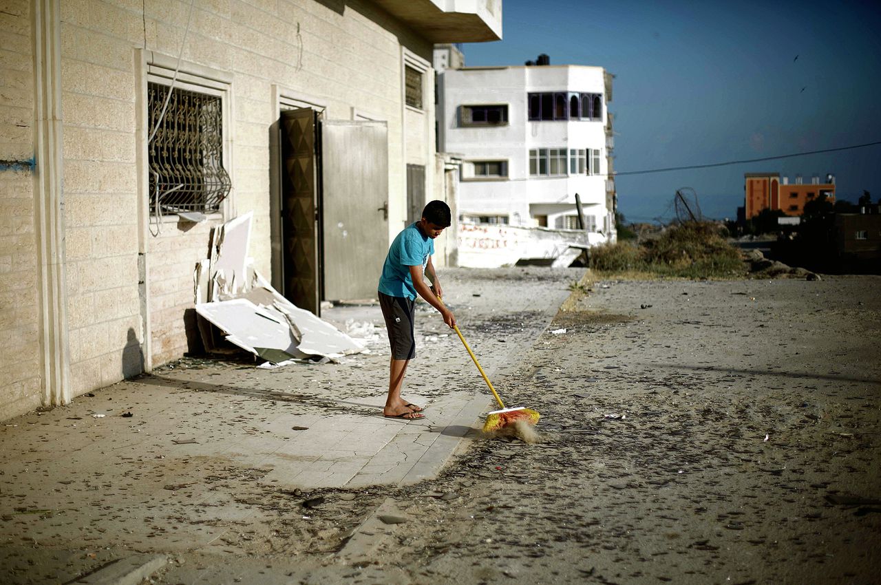 Een Palestijnse jongen maakt de stoep schoon na Israëlische bombardementen deze week op de militaire basis van Hamas. Foto MOHAMMED ABED/AFP