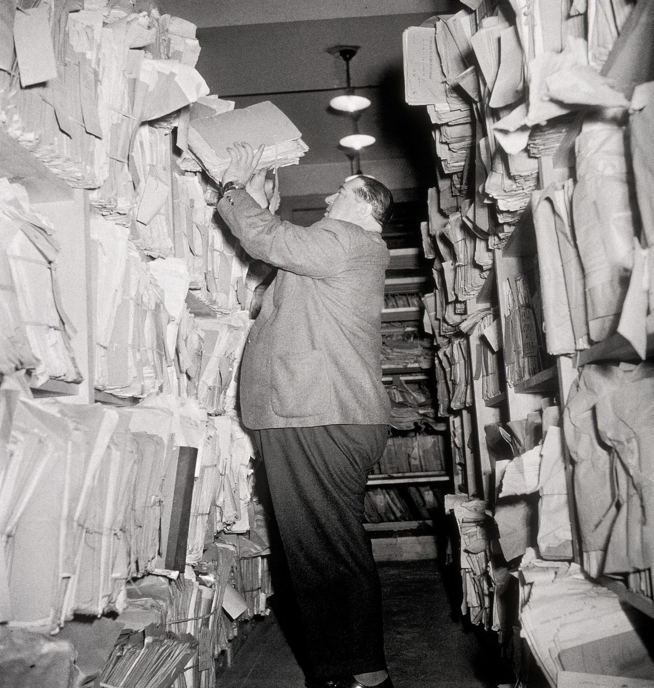 Onbekende man in een archief Foto Jupiterimages Man Stuffing Files into Overflowing Shelves