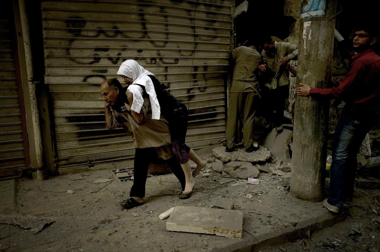 Een man draagt een vrouw weg uit haar verwoeste huis in Aleppo. Foto AFP / Zac Baillie