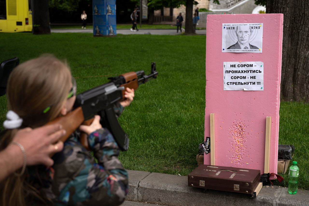 Een Oekraïens meisje schiet met haar speelgoedwapen balletjes op een portret van Poetin in Lviv.