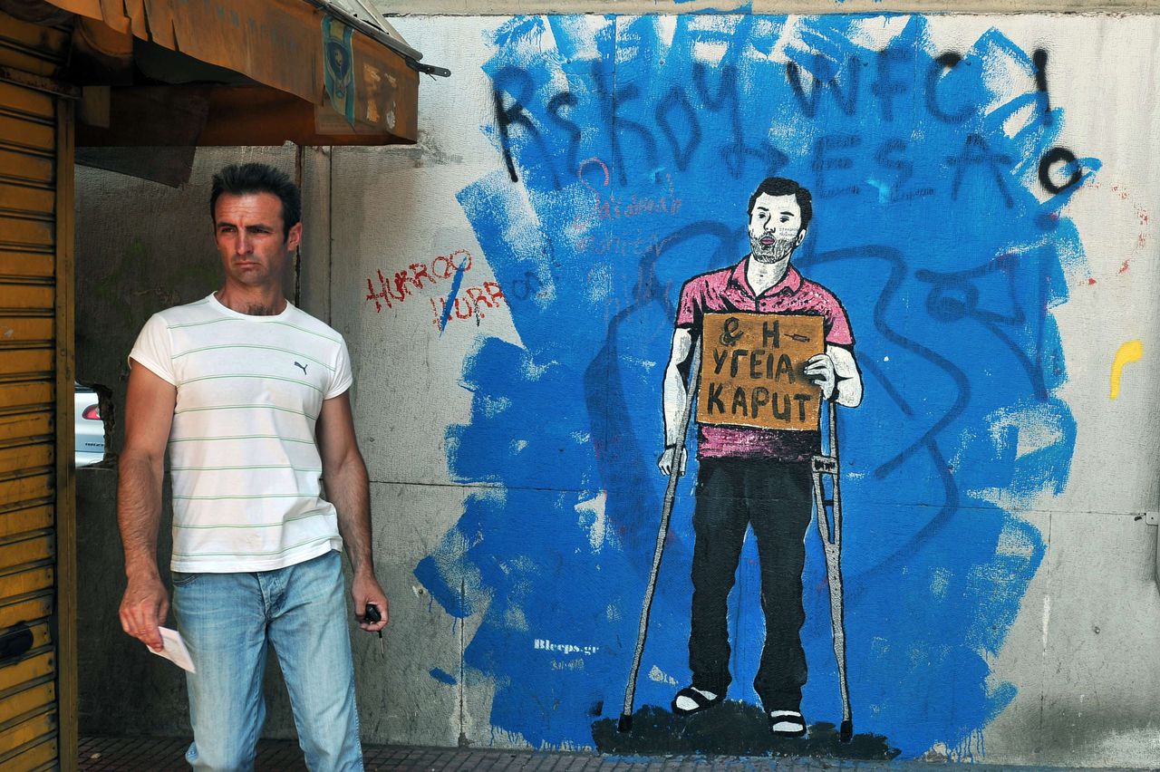 topshots TO GO WITH AFP STORY BY DARIO THUBURN A man walks by an economic-crisis related graffiti depicting a man in crutches holding a sign reading ""Health Kaput", a reference to the disrepair of the Greek public health system, on a wall in Athens on June 15, 2012. From political slogans scrawled on the walls to works of street art in run-down neighbourhoods, Greece's economic crisis is inspiring graffiti that probe acute social themes ahead of the upcoming May 17 general election. AFP PHOTO/ LOUISA GOULIAMAKI
