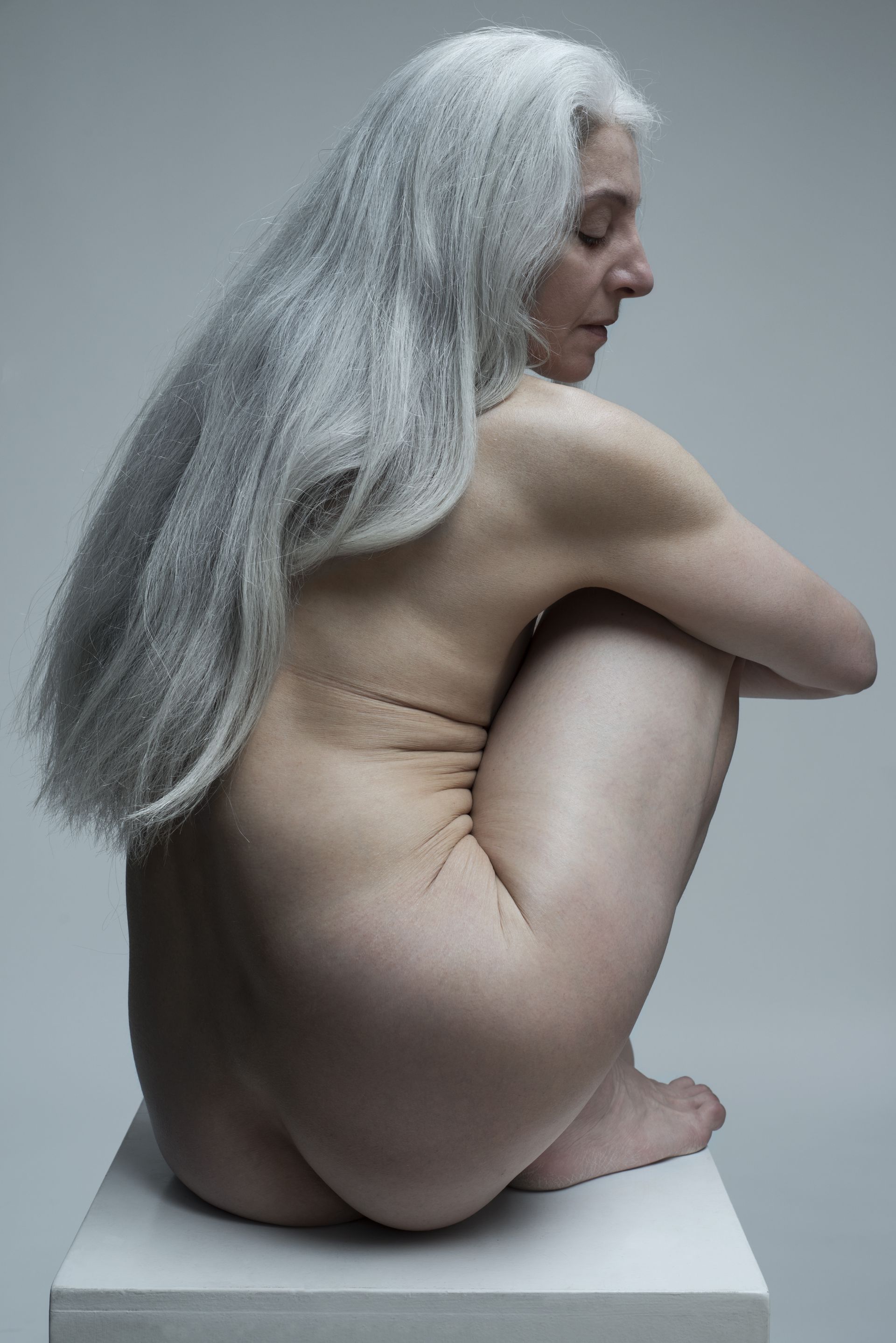 Mature naked woman sitting in studio shot. 