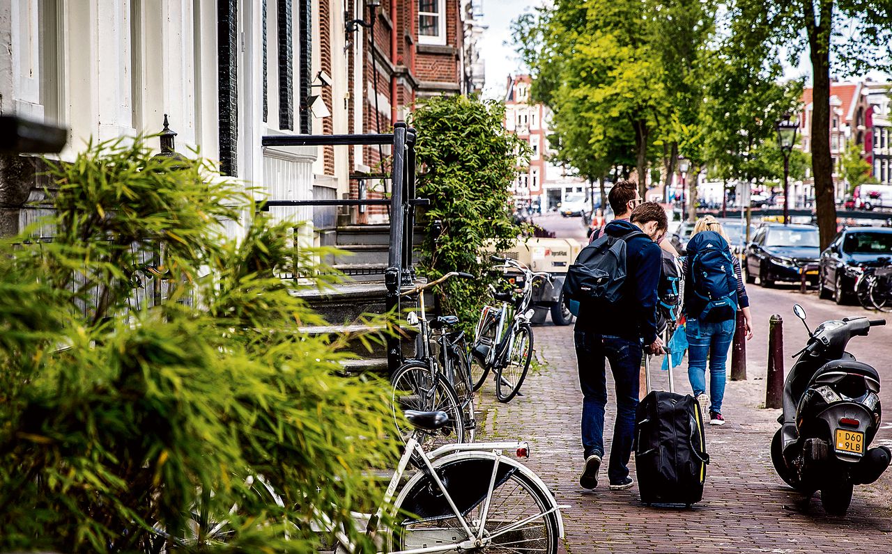 Toeristen met rolkoffers op de grachten in Amsterdam.