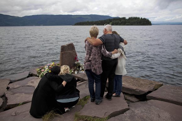 Relatives of a victim gather to observe a minute's silence on a campsite jetty on the Norwegian mainland, across the water from Utoya island, seen in the background, where people have been placing floral tributes in memory of those killed in the shooting massacre on the island, Monday, July 25, 2011. An Oslo district court judge decides to hold the arraignment for the suspect in the twin attacks in Norway behind closed doors, depriving him of the platform he's looking for to air his belief that Europe must be saved from Muslim colonization. (AP Photo/Matt Dunham)