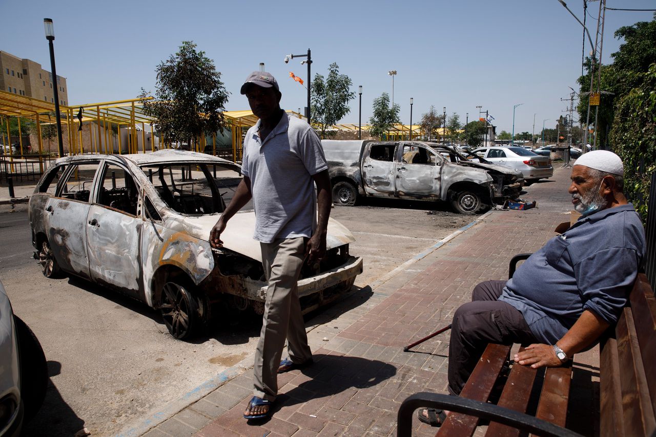 Een voorbijganger loopt woensdag langs uitgebrande auto’s in de Israëlische stad Lod.