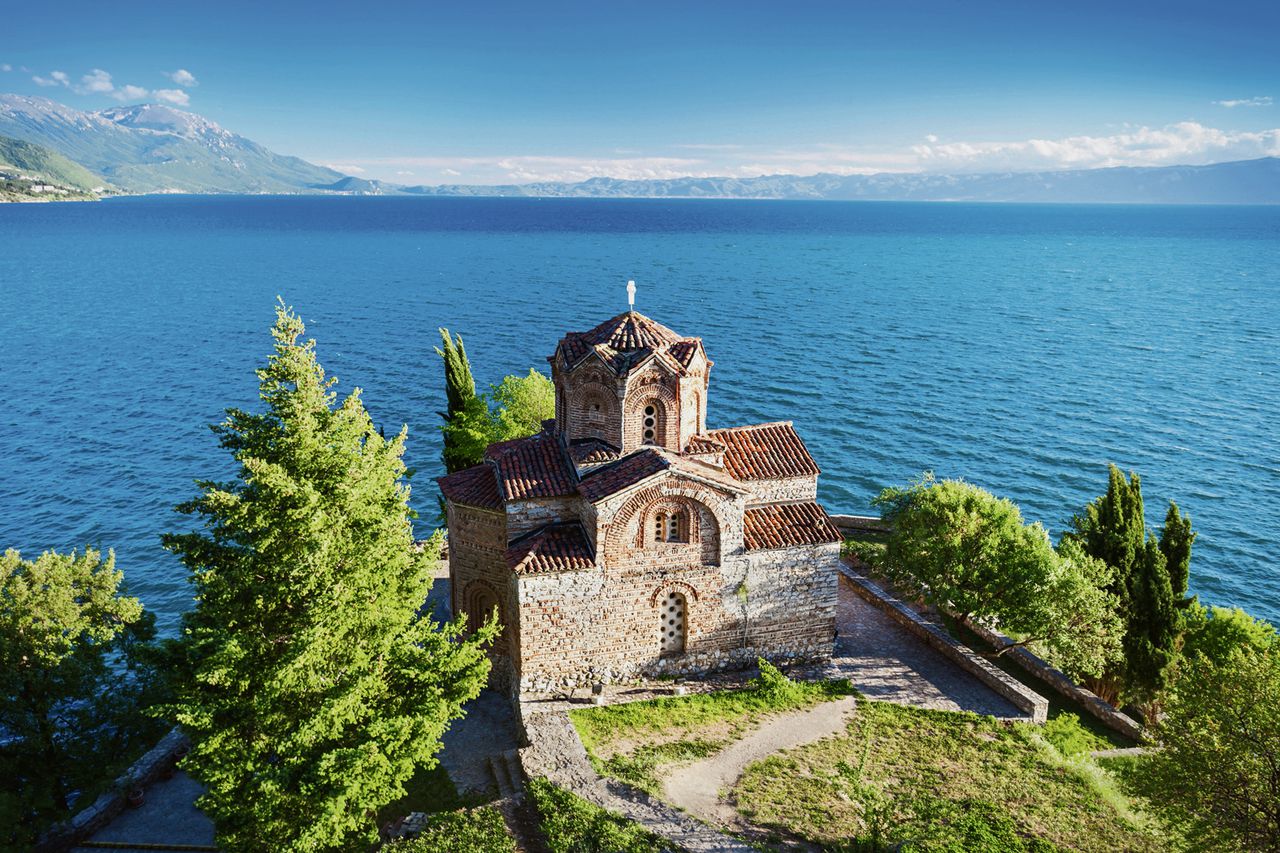 „En op dit uiterste puntje van Ohrid's vestingheuvel, vlak tegen de rand van de laatste rotsbank, die steil in het water valt, angstvallig verwijderd van de laatste, toch al doodstille en schijnbaar onbewoonde huizen, stond een kleine kerk, alleen met rots, wind en water.” - citaat uit ‘De bruiloft der zeven zigeuners’