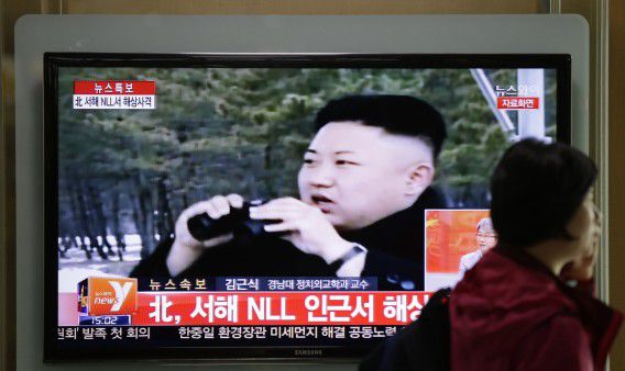 Een vrouw loopt langs een televisiescherm over de schietoefeningen. Op de beelden is de Noord-Koreaanse leider Kim Jong-un te zien.
