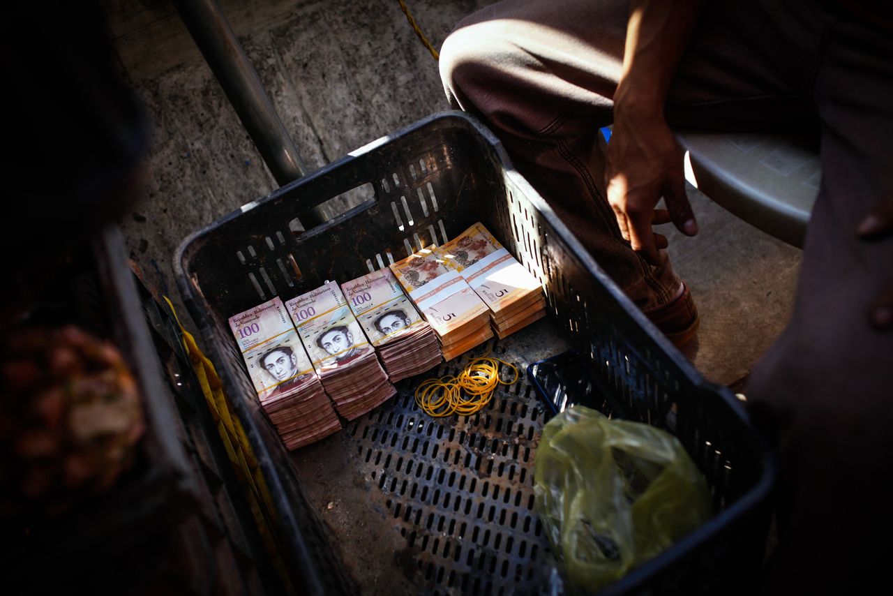 Een fruitverkoper op de markt van Caracas heeft de stapels bankbiljetten van 50 en 100 bolívar opgestapeld in een krat. Door hyperinflatie is er een groot tekort aan contant geld in Venezuela, dat vandaag naar de stembus gaat.